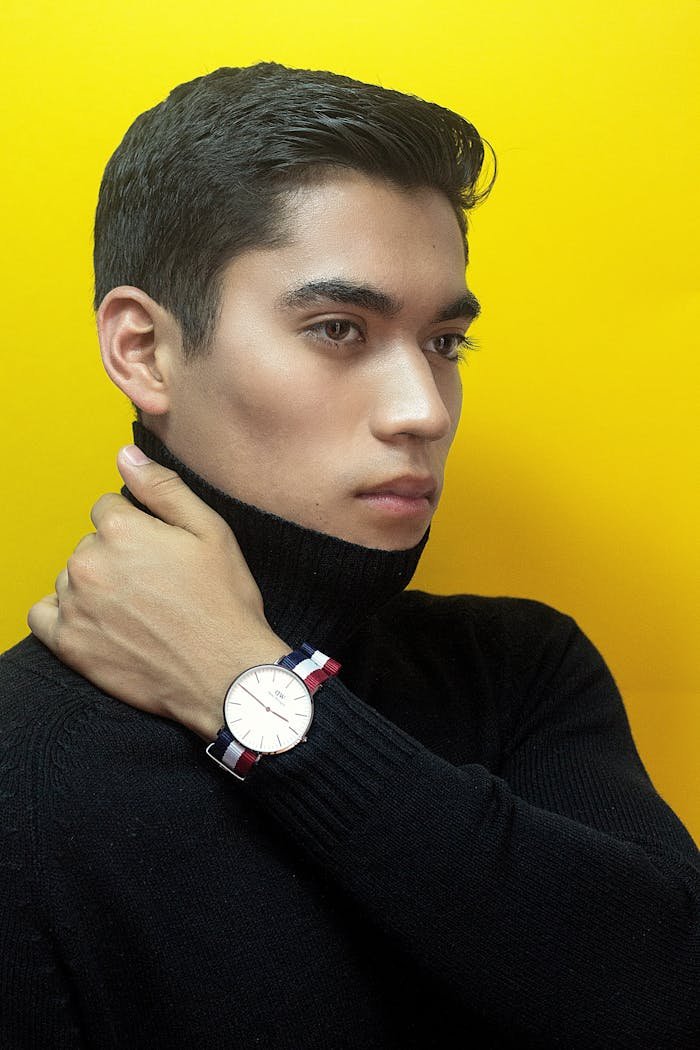 Portrait of a stylish man wearing a wristwatch and black sweater against a vibrant yellow backdrop.